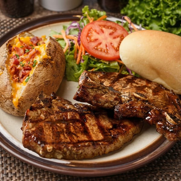 Two charbroiled steaks with a loaded baked potato, side salad, and bread roll on a plate.