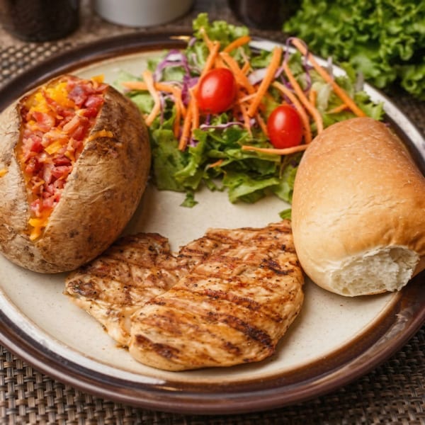 Grilled chicken breast, baked potato with cheese and bacon, side salad, and a bread roll.