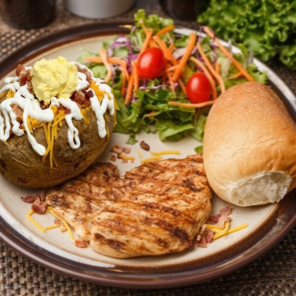 Grilled chicken, a loaded baked potato, a side salad with tomatoes, and a dinner roll.